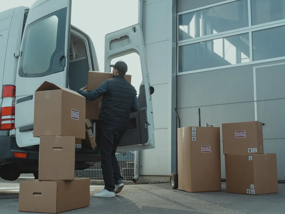 Courier loading boxed deliveries into a white cargo van outside a commercial building